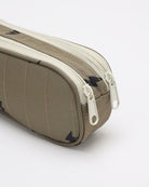 A close-up of a taupe-colored zippered pouch or pencil case with a textured surface and white zipper pulls, shown on a light gray background.