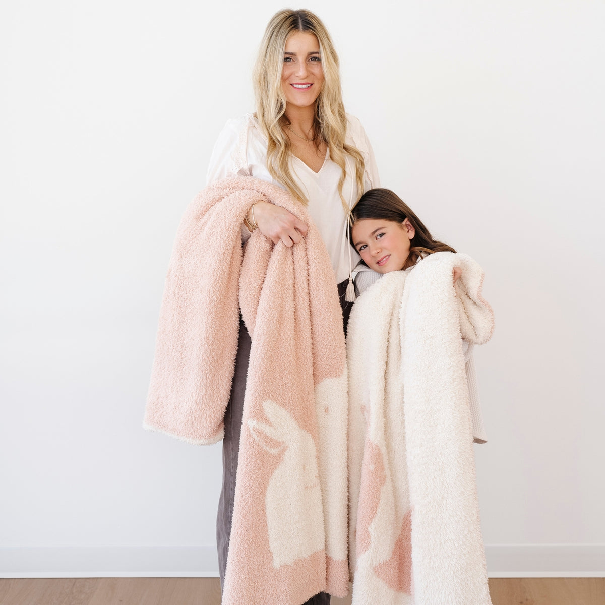 Woman and child holding pink and white fuzzy blankets against a white background