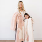 Woman and child holding pink and white fuzzy blankets against a white background