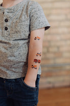 Child with temporary tattoos of trucks on their arm against a brick wall background