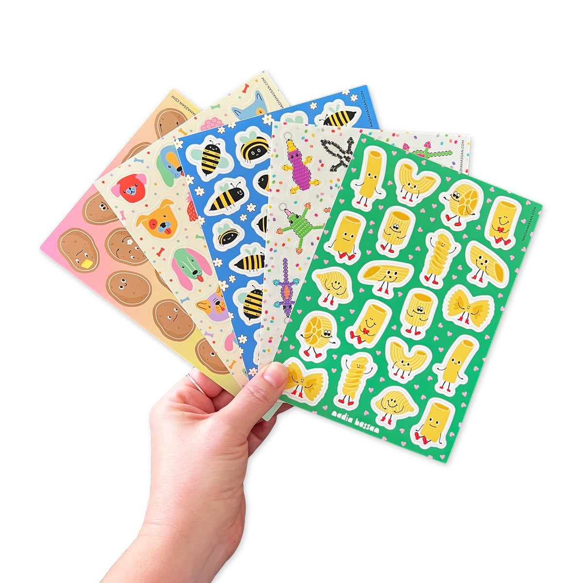 Hand holding a set of colorful sticker sheets with various designs on a white background