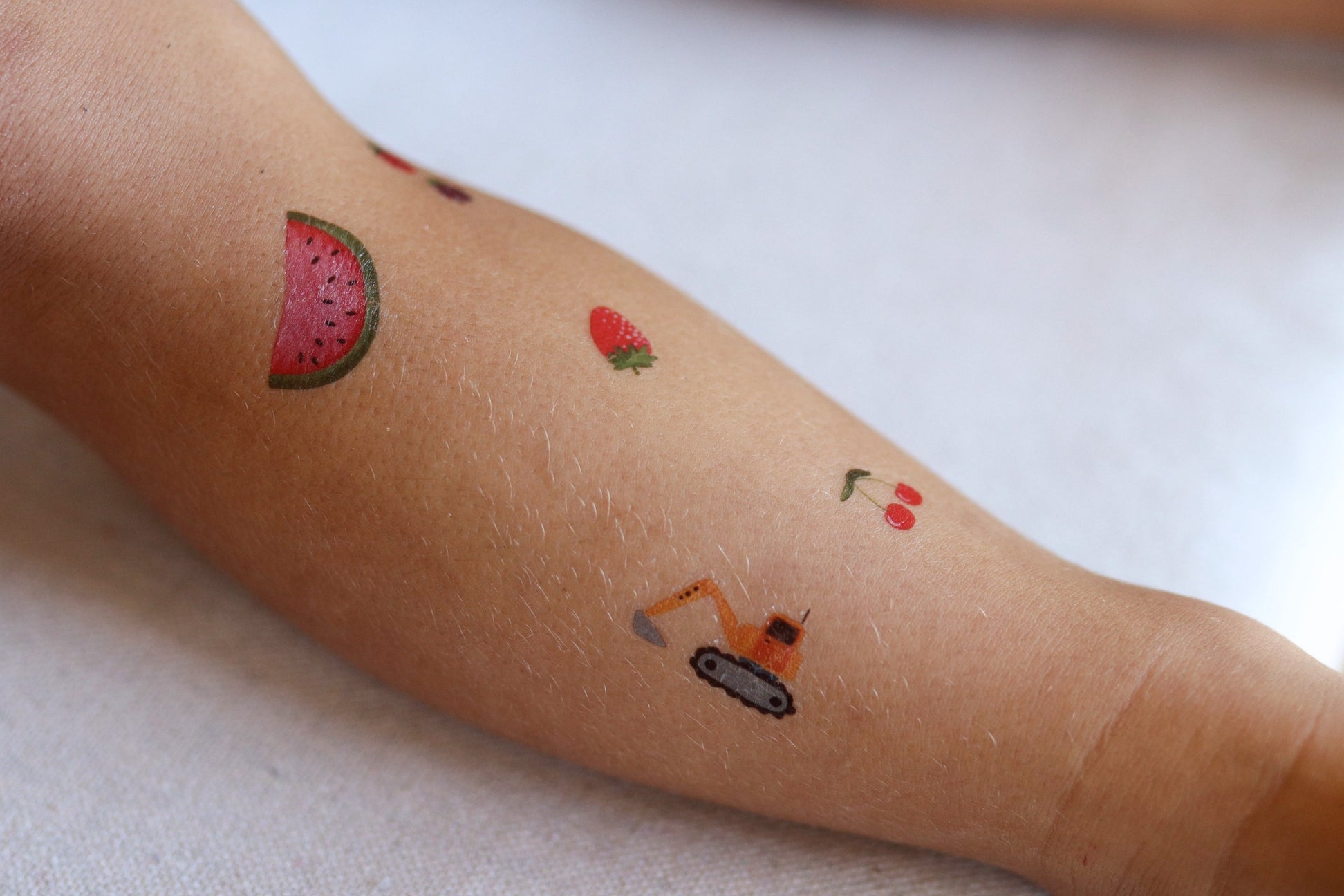 Small tattoos of a watermelon slice, strawberry, cherry, and robot on a person's arm.