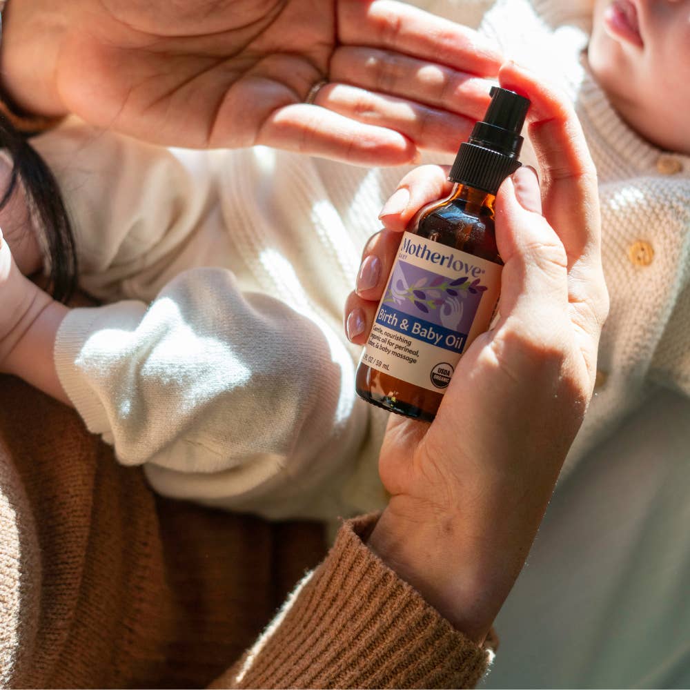 Person holding a bottle of Motherlove Earth & Baby Oil with a child in the background