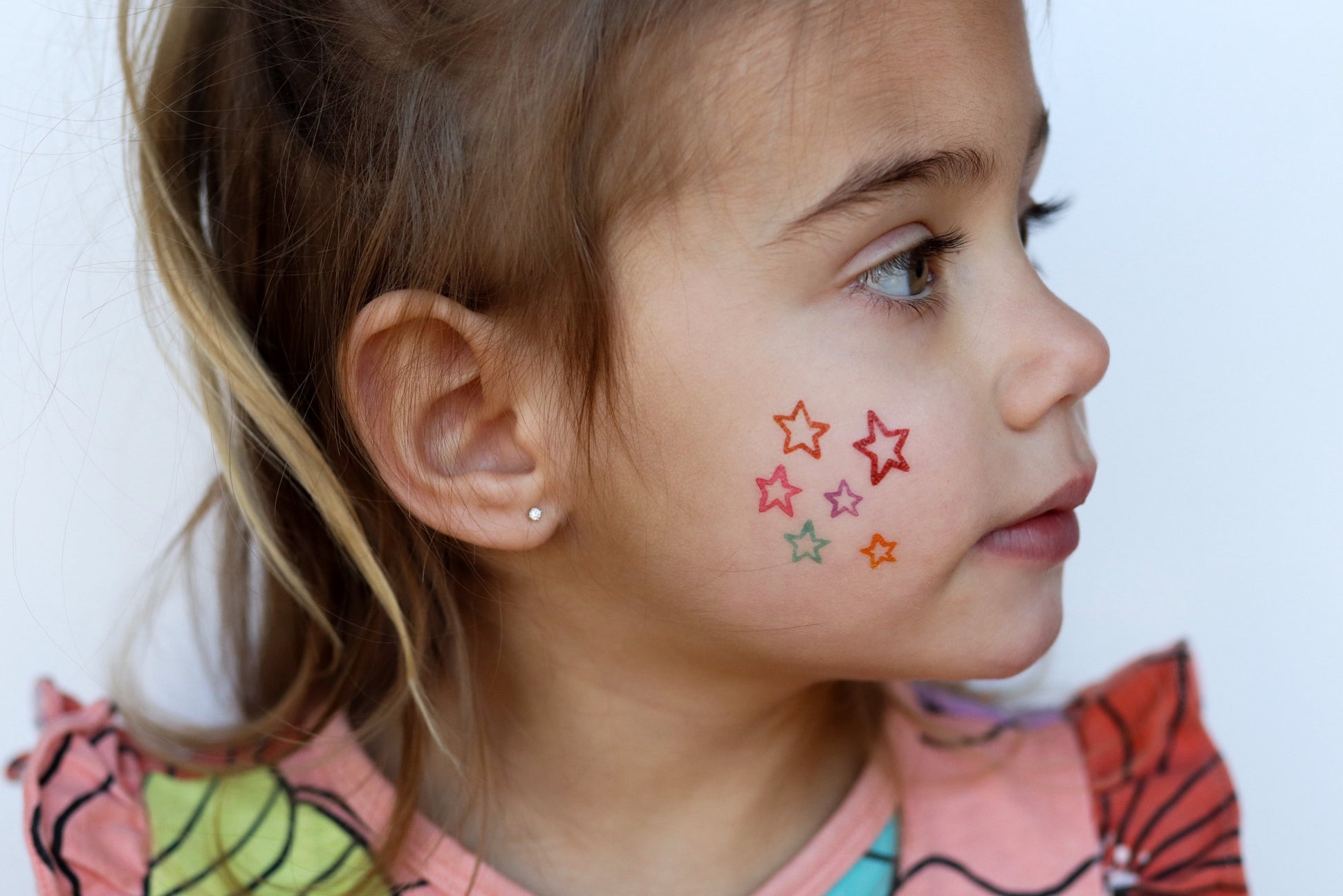 Young girl with colorful star tattoos on her face against a white background