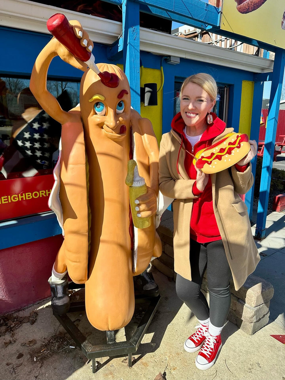 Person in a costume holding a hot dog with mustard and ketchup next to a large hot dog statue.