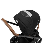 A close-up profile view of the black MIXX Next + Pipa Aire RX Travel System by Nuna stroller showing the brown leatherette handlebar and canopy with a mesh ventilation window, set against a checkered transparent background.