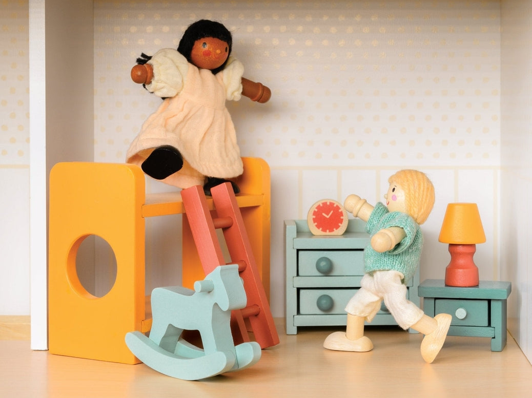 Wooden doll figure climbing down the ladder of a yellow bunk bed in a miniature room setting with a slide, light blue rocking horse, chest of drawers, and bedside table with a lamp.