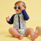 Baby wearing a patterned outfit and sunglasses on a yellow background