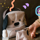 Baby car seat with a dog design, hand reaching towards it on a wooden surface.
