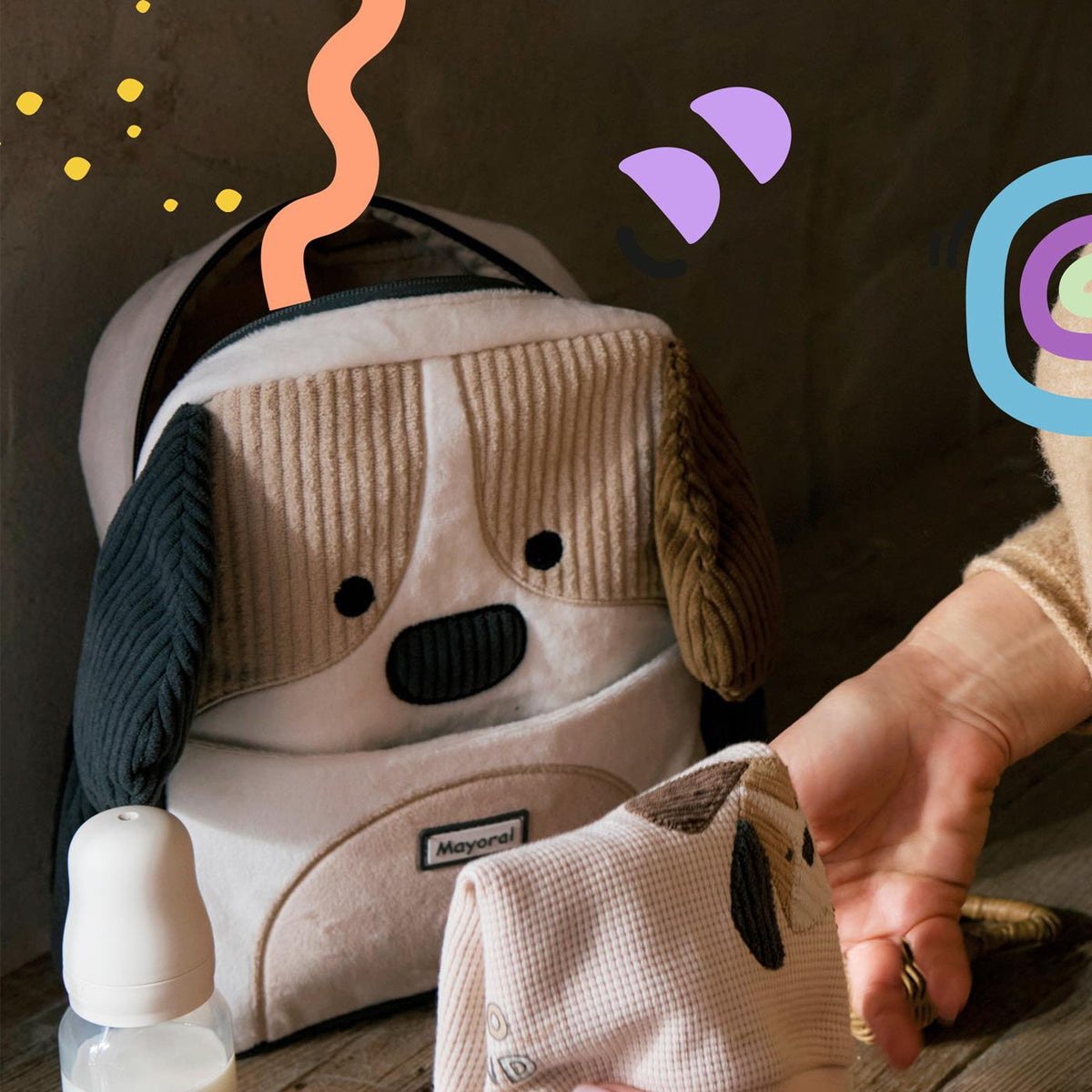 Baby car seat with a dog design, hand reaching towards it on a wooden surface.