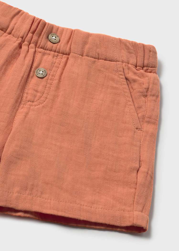 Close-up of terracotta shorts with button details on a light gray background