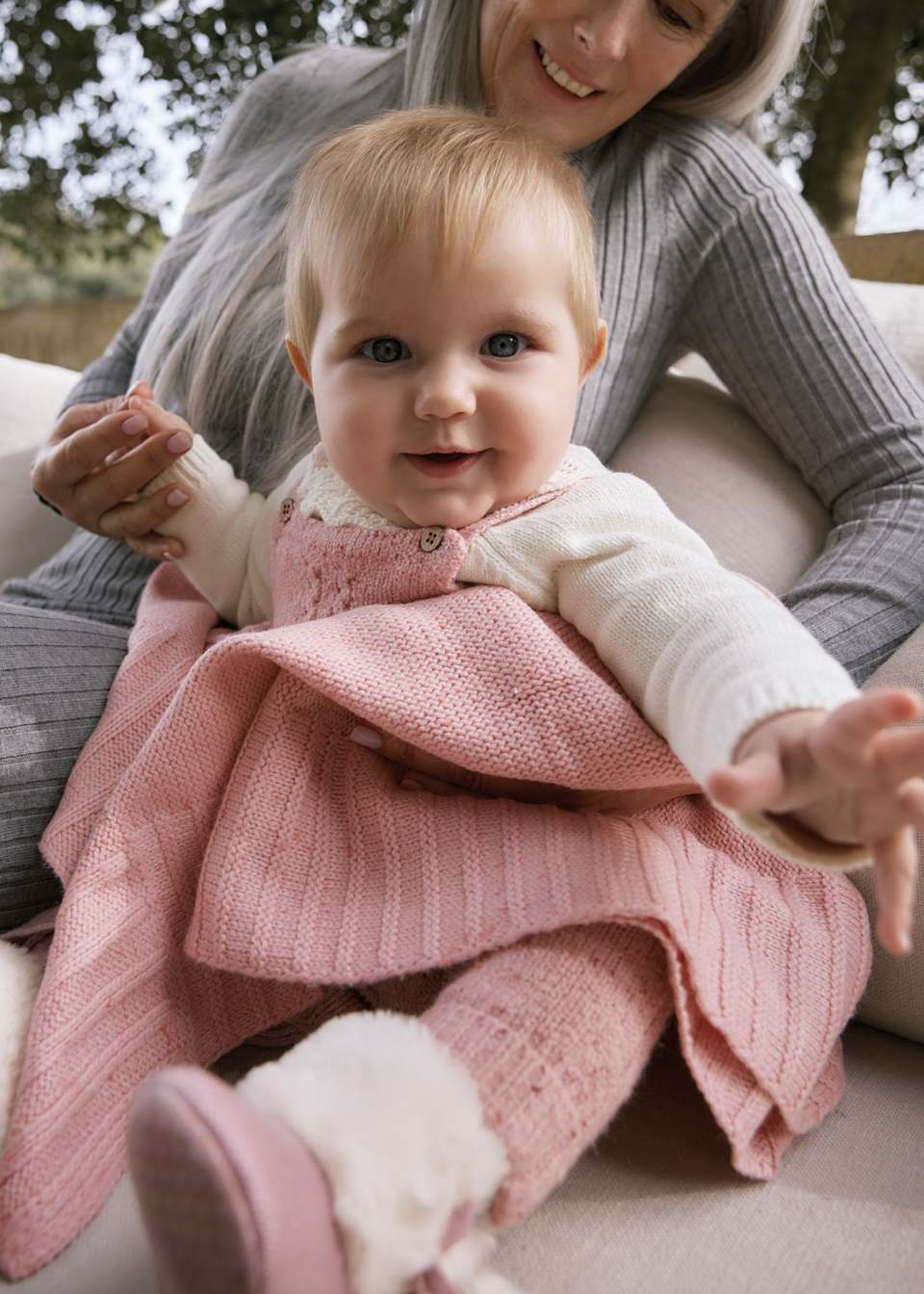 Woman holding a baby wrapped in a pink blanket outdoors