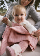 Woman holding a baby wrapped in a pink blanket outdoors