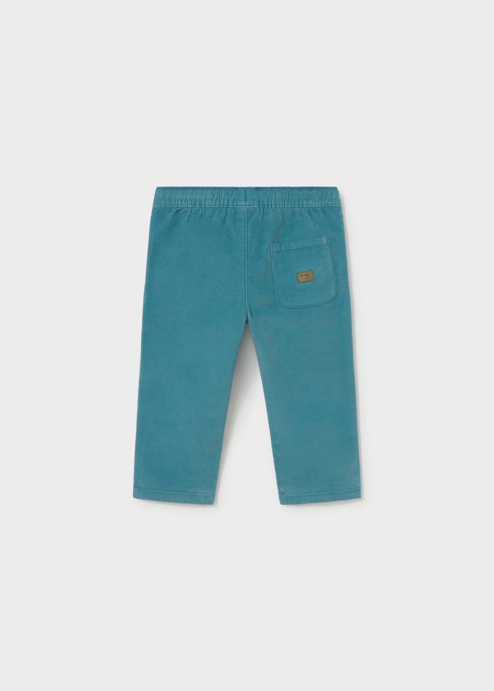 A pair of teal corduroy pants for toddlers, shown from the back on a light gray background. The back features an elastic waistband, straight legs, and a single patch pocket on the right side with a small brown brand label.