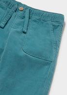 Teal pants with a button and strap on a light gray background