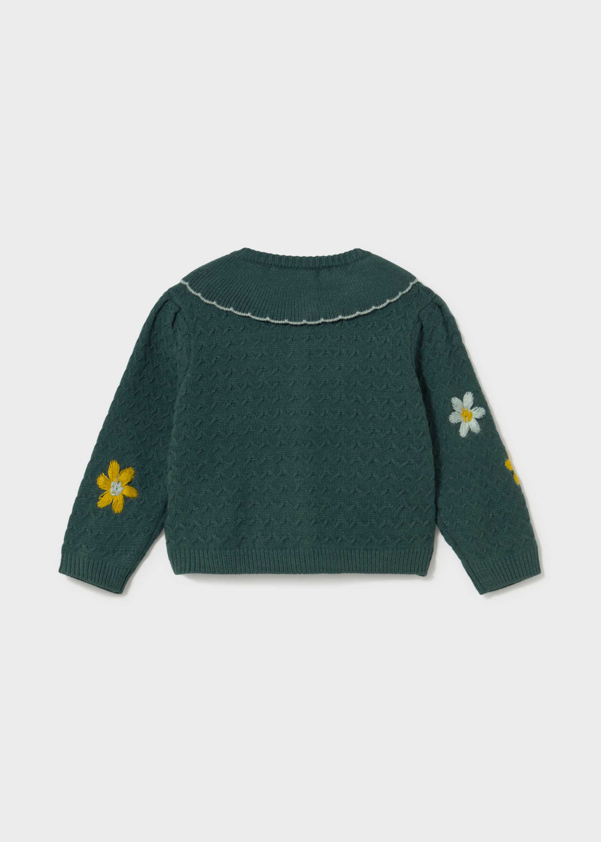 A dark green knit sweater shown from the back, featuring a scalloped collar, textured knit pattern, and embroidered daisy flowers on the sleeves against a light gray background.