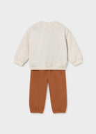 A two-piece children's outfit set featuring a long-sleeve crewneck sweatshirt in a light oatmeal cream color and matching jogger pants in a warm rust orange, shown from the back on a light gray background.
