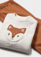 Folded white sweatshirt with a fox face design on a brown fabric background