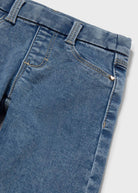 Close-up of blue denim jeans showing the waistband, belt loops, front pocket, and stitching details against a light gray background.
