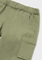 Close-up of olive green pants showing the elastic waistband, side pocket, and cargo-style flap pocket on a light gray background.