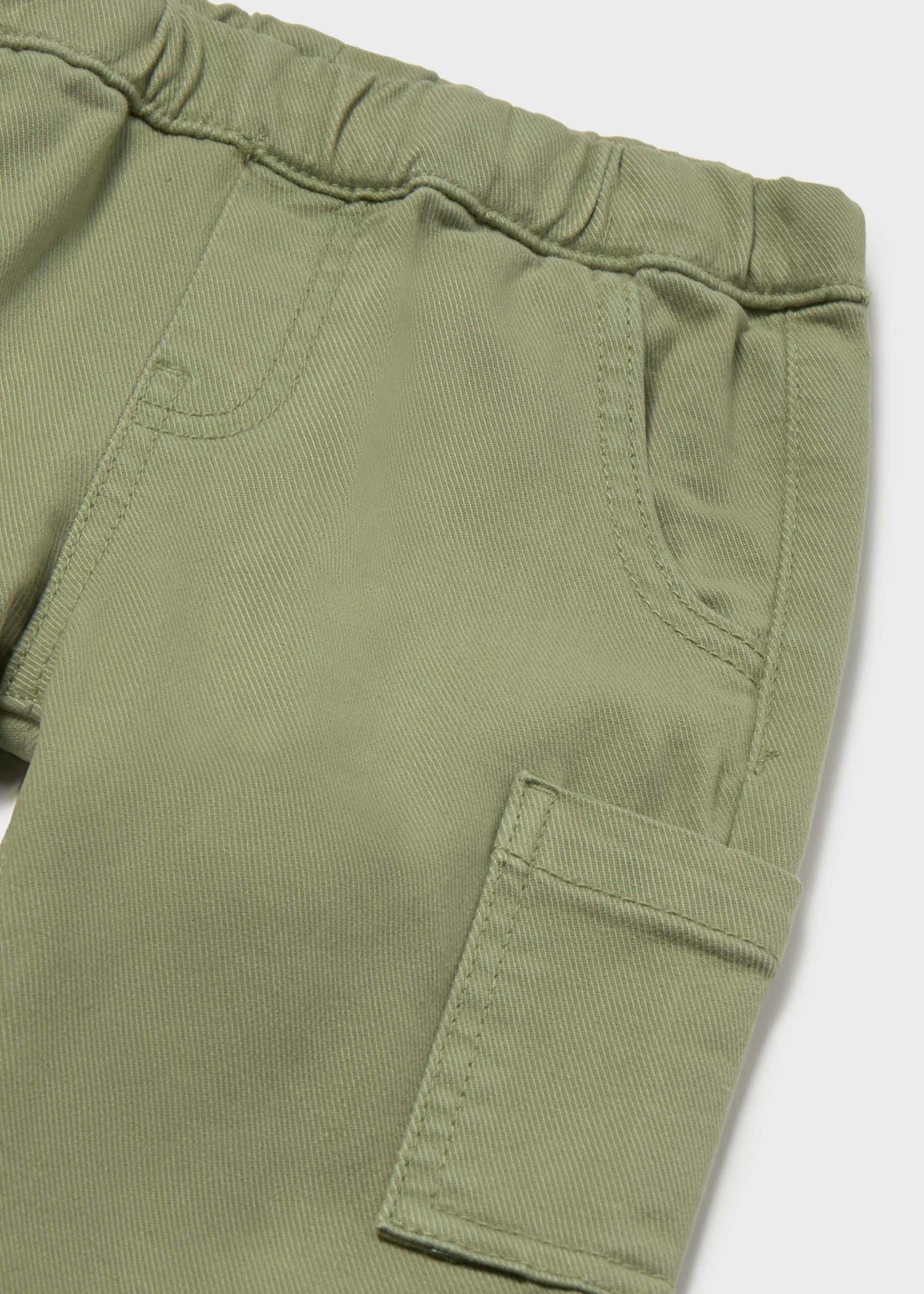 Close-up of olive green pants showing the elastic waistband, side pocket, and cargo-style flap pocket on a light gray background.