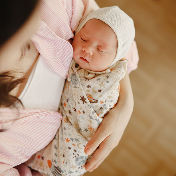 Newborn baby wrapped in a patterned blanket and wearing a hat, held by a person.