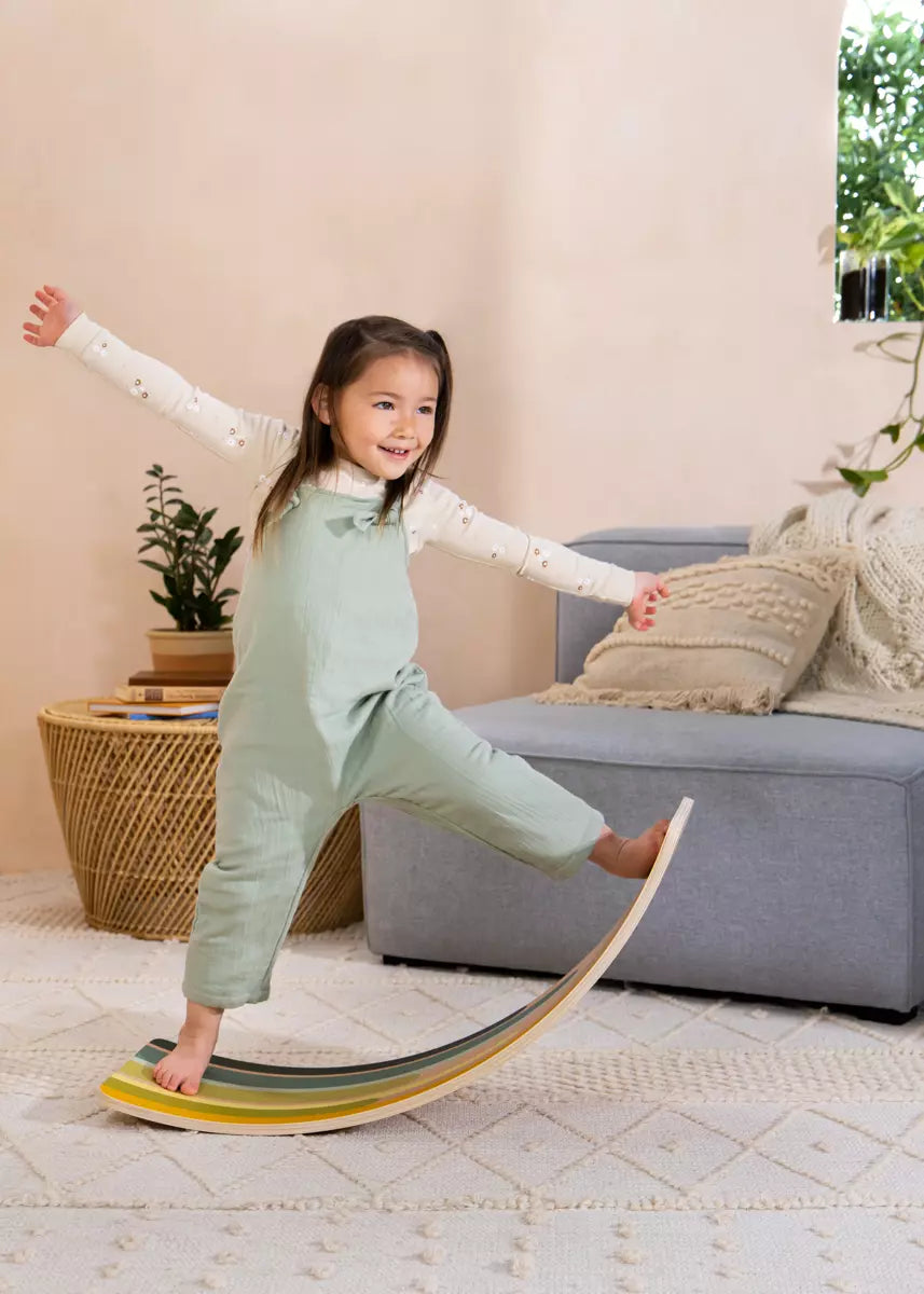 Child balancing on a wooden balance board in a living room.