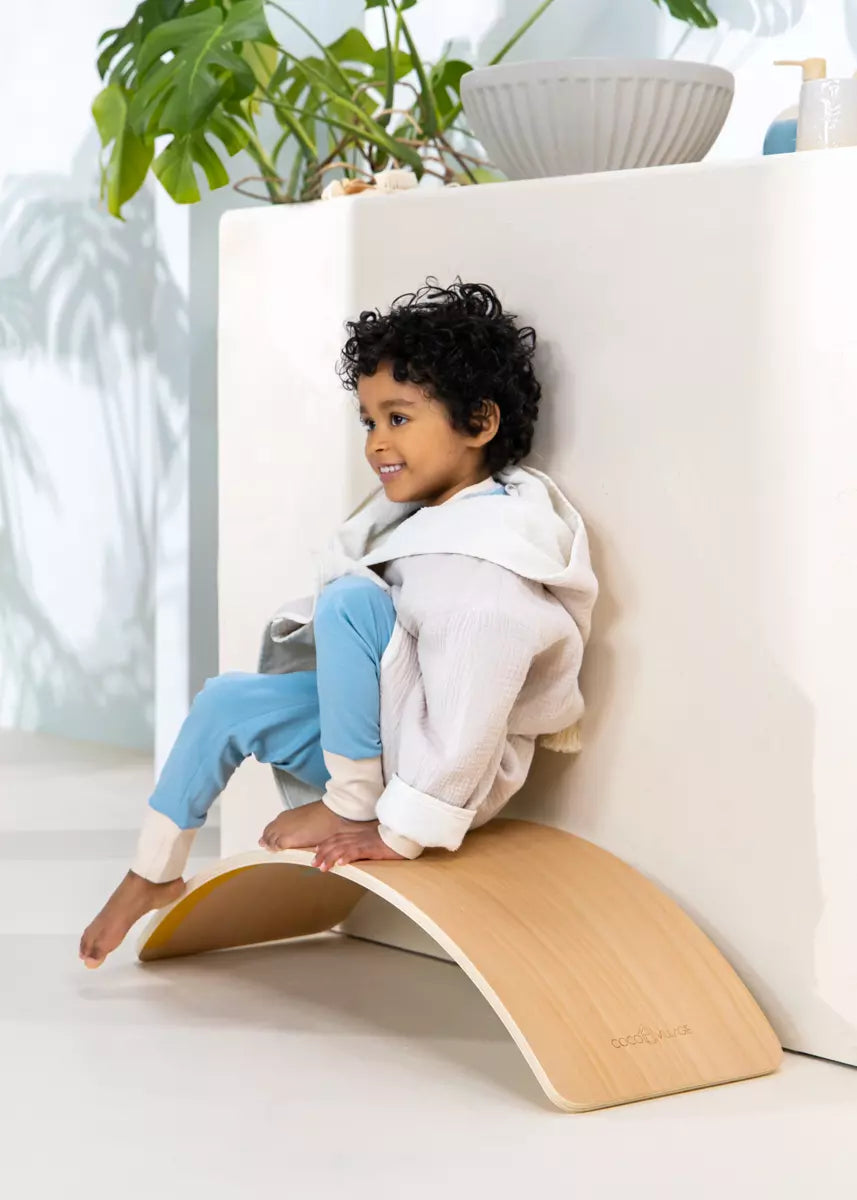 Child sitting on a wooden wobble chair in a bright room with plants