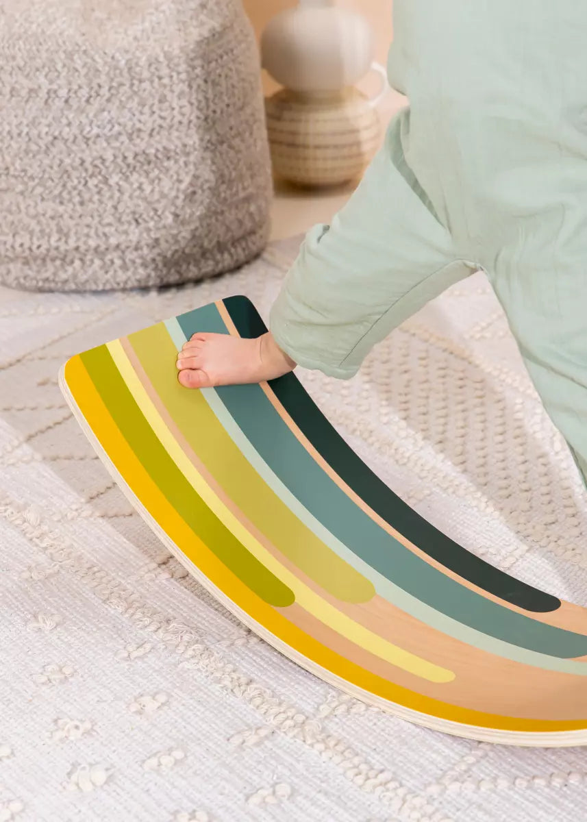 Child's hand on a colorful wooden balance board on a textured floor.