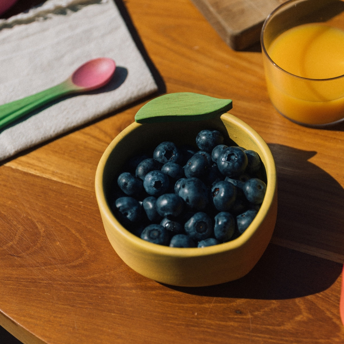 Yellow bowl with blueberries on a wooden table next to a glass of orange juice.