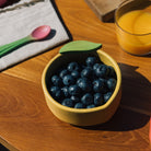 Yellow bowl with blueberries on a wooden table next to a glass of orange juice.