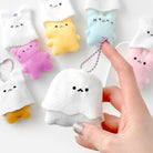 Hand holding a small plush ghost toy with colorful plush toys in the background.
