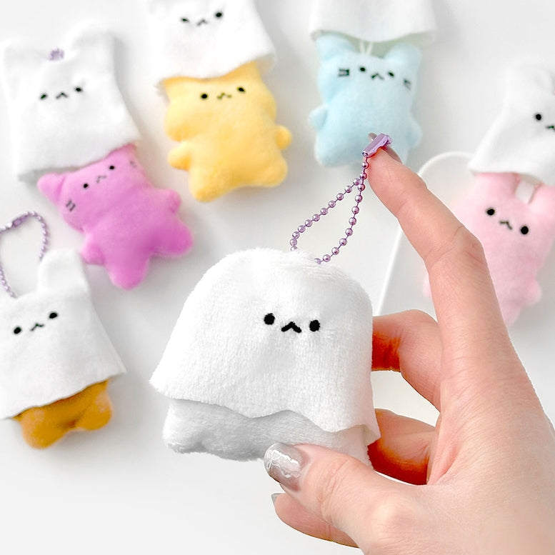 Hand holding a small plush ghost toy with colorful plush toys in the background.