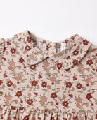 Close-up of a children's dress with a ruffled Peter Pan collar and a dusty floral print on a light beige linen-like fabric, featuring red and brown flowers with green leaves.
