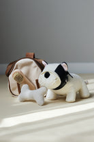 Stuffed dog toy with a bone and a doghouse on a light surface with a gray background