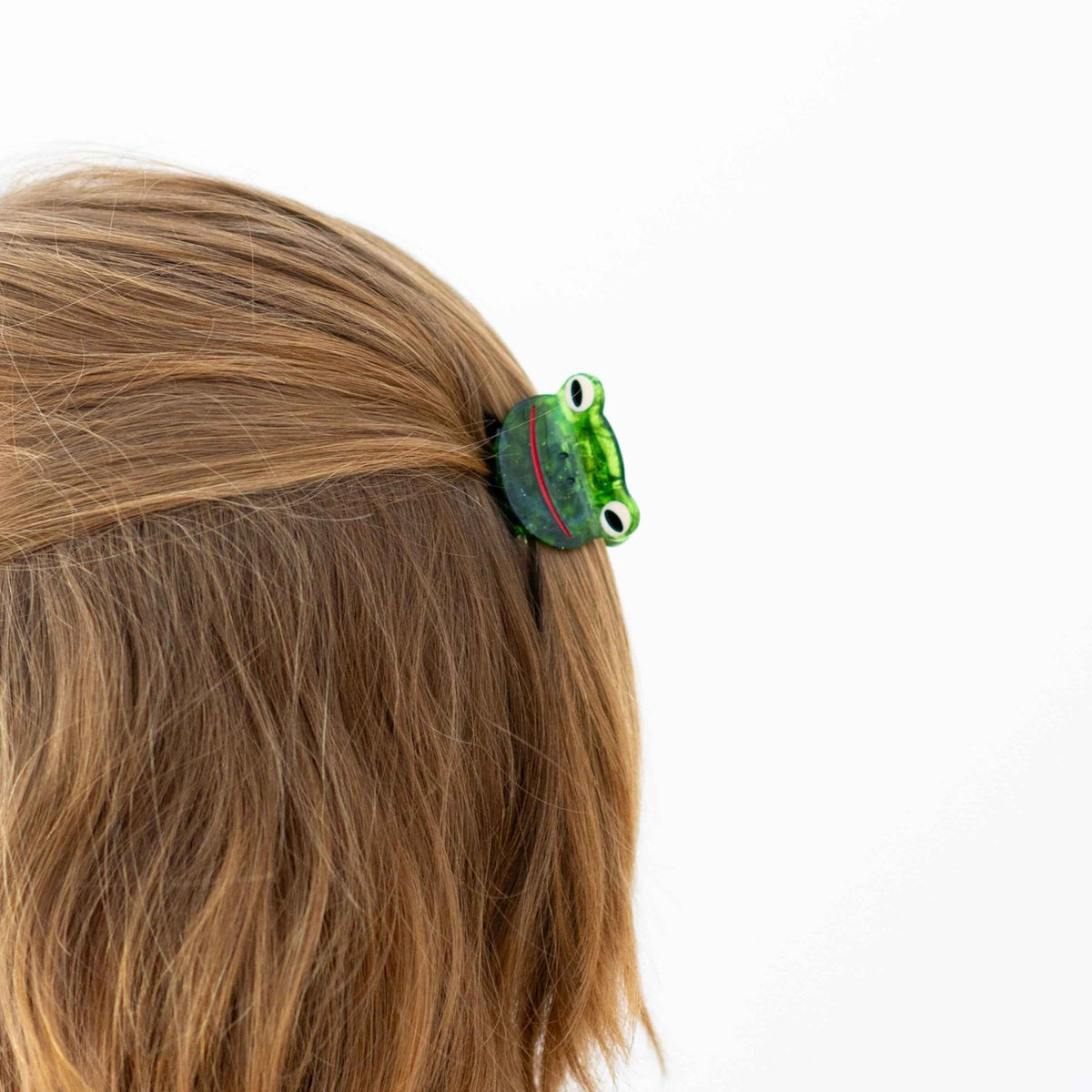 Green frog-shaped hair clip on a person's head with a white background