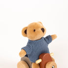 Teddy bear in a blue sweater sitting on a wooden toy with a plain background