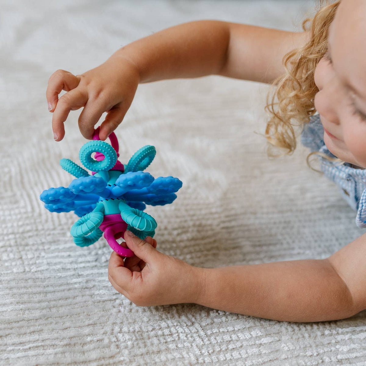 Child holding a blue and pink textured toy on a soft surface