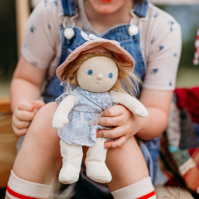 Child holding a doll with a pink hat and blue dress