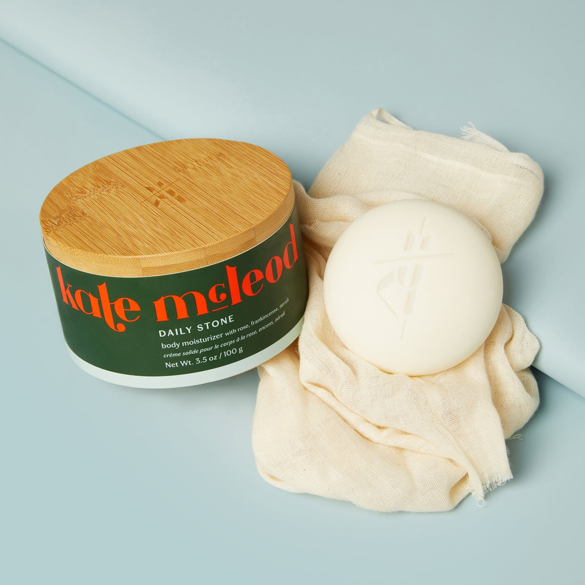 Body moisturizer jar with wooden lid and towel on a light blue background