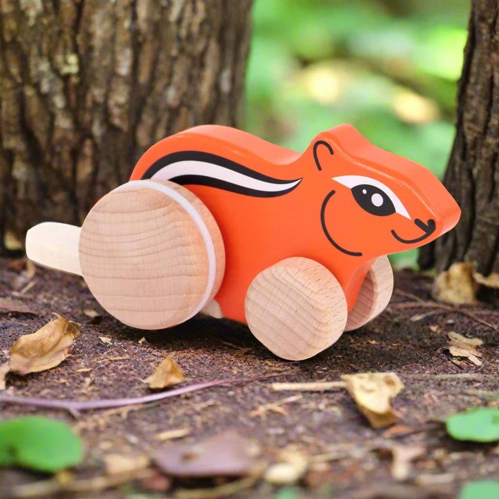 Wooden chipmunk toy with wheels on a forest floor