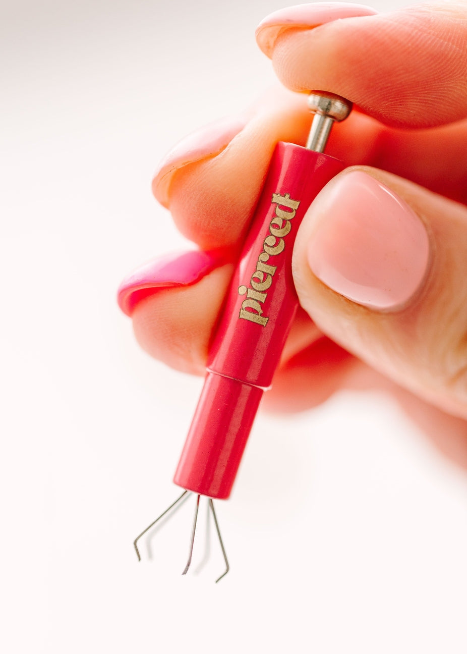 Red piercing tool with 'Periear' branding held by a hand against a white background