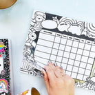 Hand holding a coloring page with a grid and decorative elements on a light blue surface.