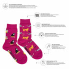 A pair of bright pink crew socks with a playful cartoon pattern of black cats, yellow lions, and white elephants walking along the sides. The image is presented on a white background with informational callouts detailing the product's features, such as 'Yarn Blend Extension' and 'High Needle Count'.
