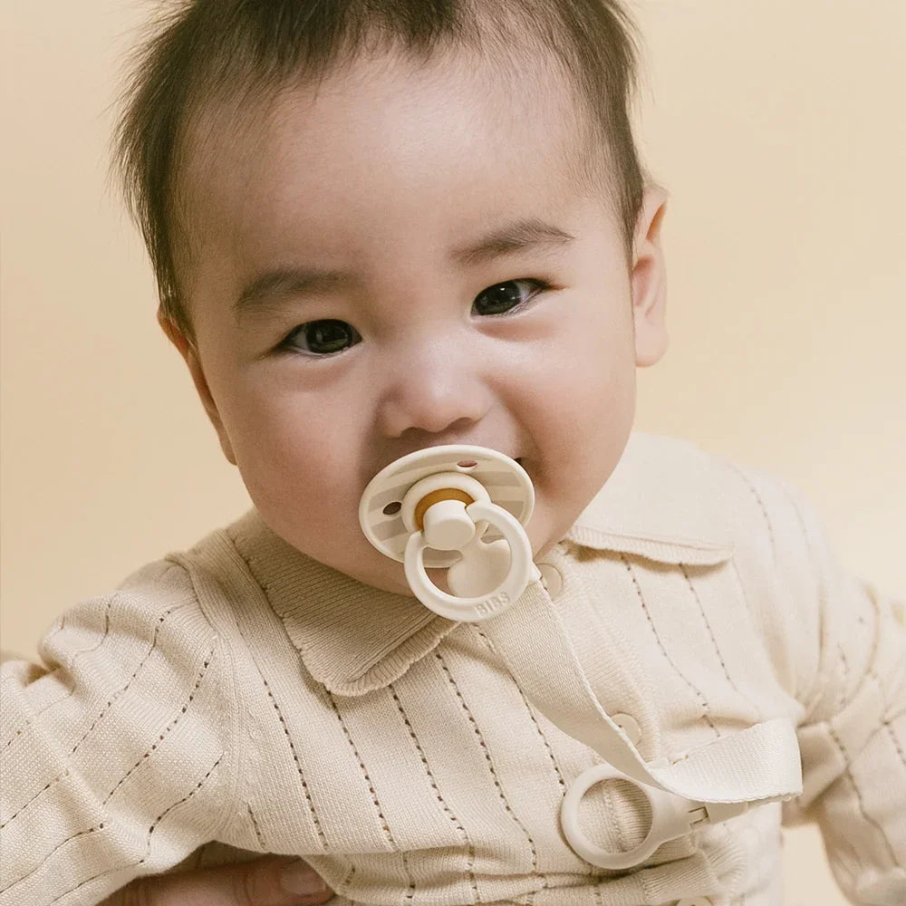 Baby wearing a beige outfit with a pacifier against a beige background
