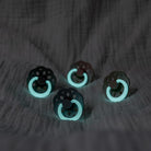 Four black and teal pacifiers on a textured dark surface