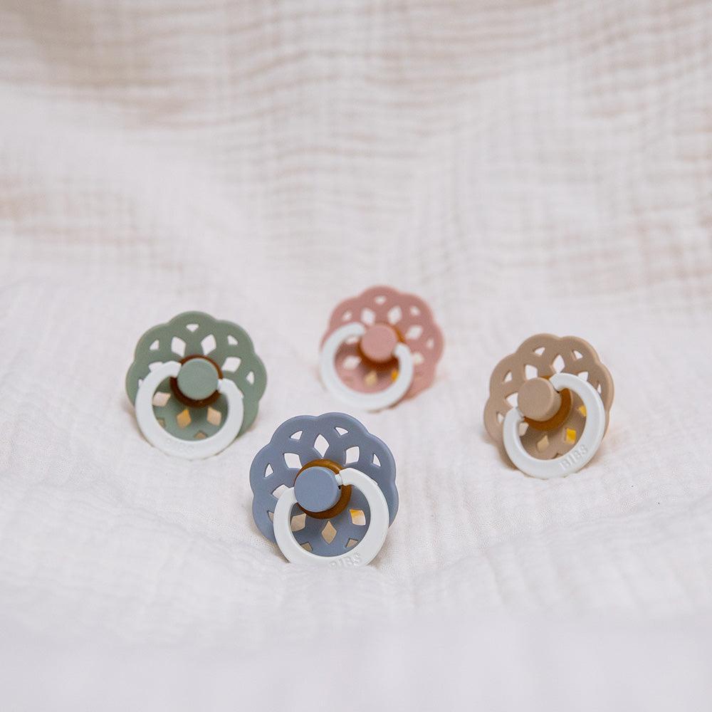 Set of four colorful baby pacifiers on a textured beige background