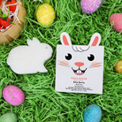 Bunny-shaped product and packaging on a grass-like surface with Easter eggs around