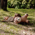 Child lying on grass with a large teddy bear in a park setting