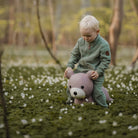 Child playing with a purple teddy bear in a forest with white flowers on the ground